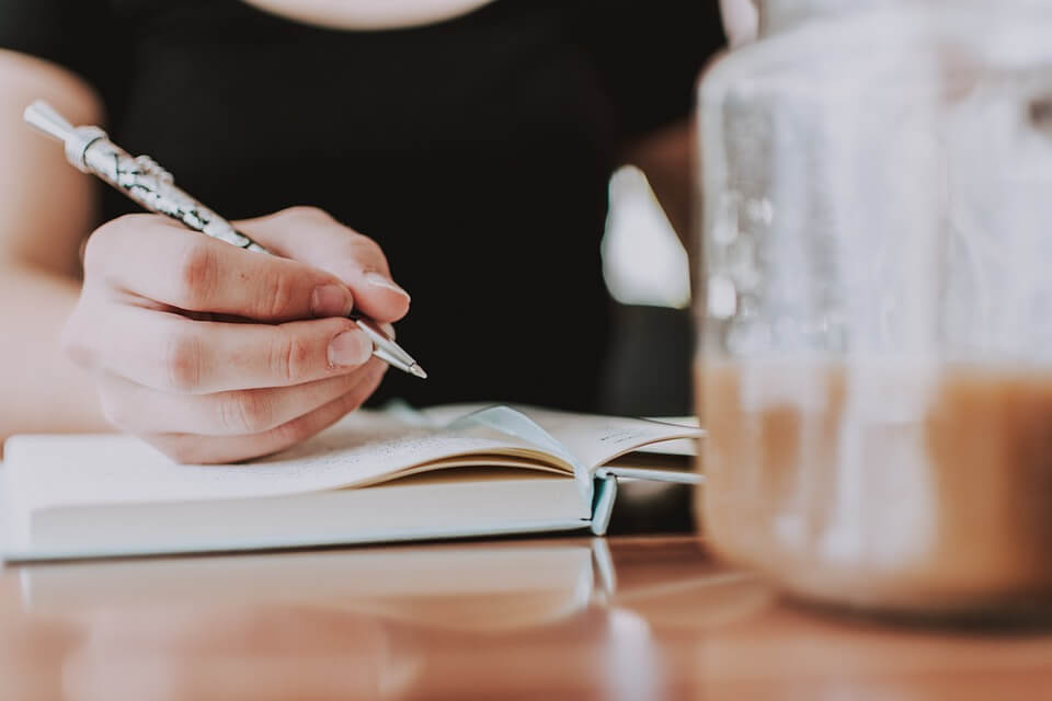 A person writing into a journal with a pen.