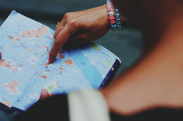 Someone is holding a paper map, and pointing at a location with a finger.