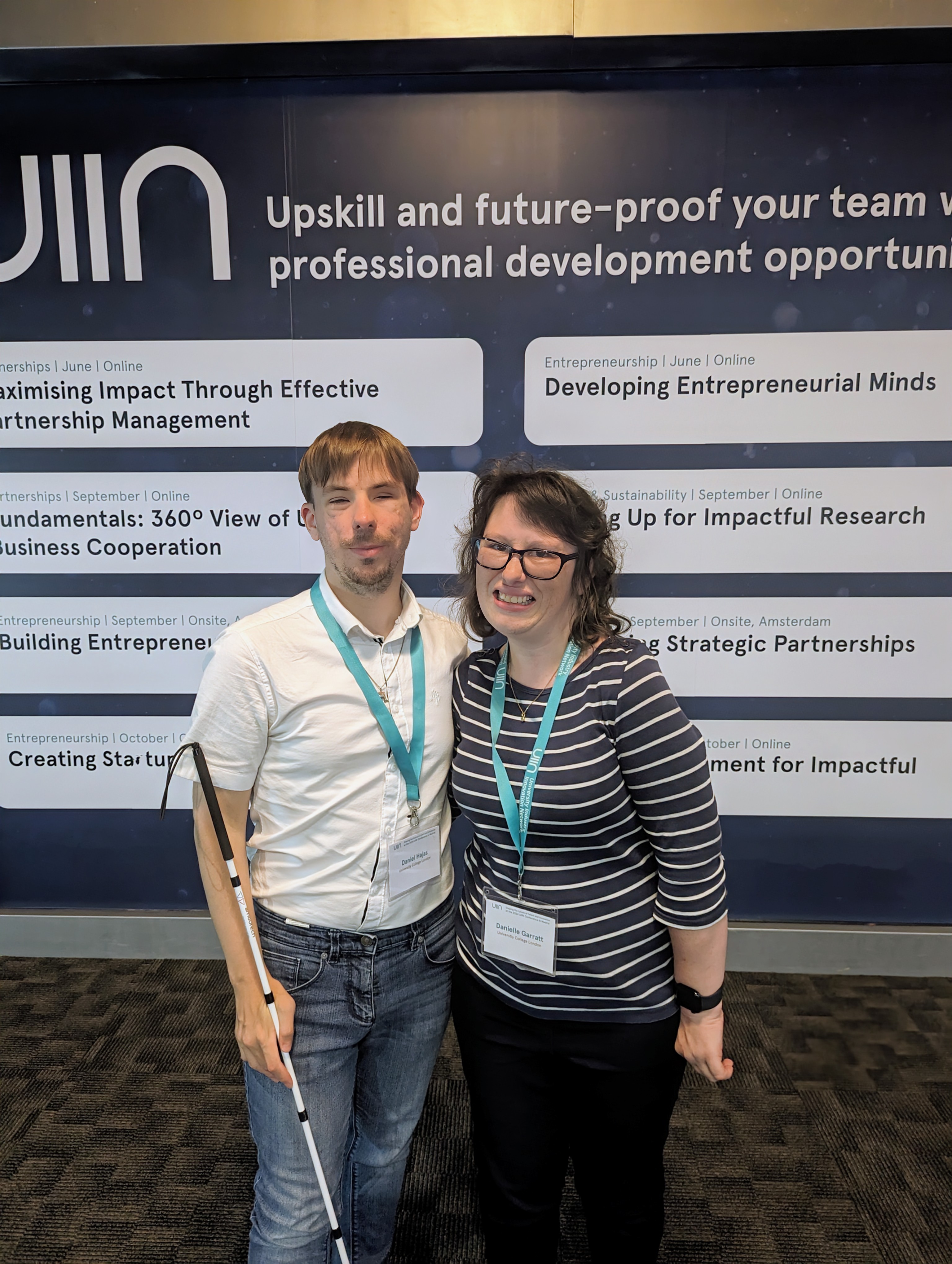 Daniel and Danielle are standing in front of a wall displaying eight speechbubbles. The following text is visible, 'Impact through effective partnership management',  'Fundamentals 360 view of business cooperation', 'business entrepreneurship', 'Creating startups', 'Developing entrepreneurial minds', 'Up for impactful research', 'Strategic partnerships' and 'for impact'.